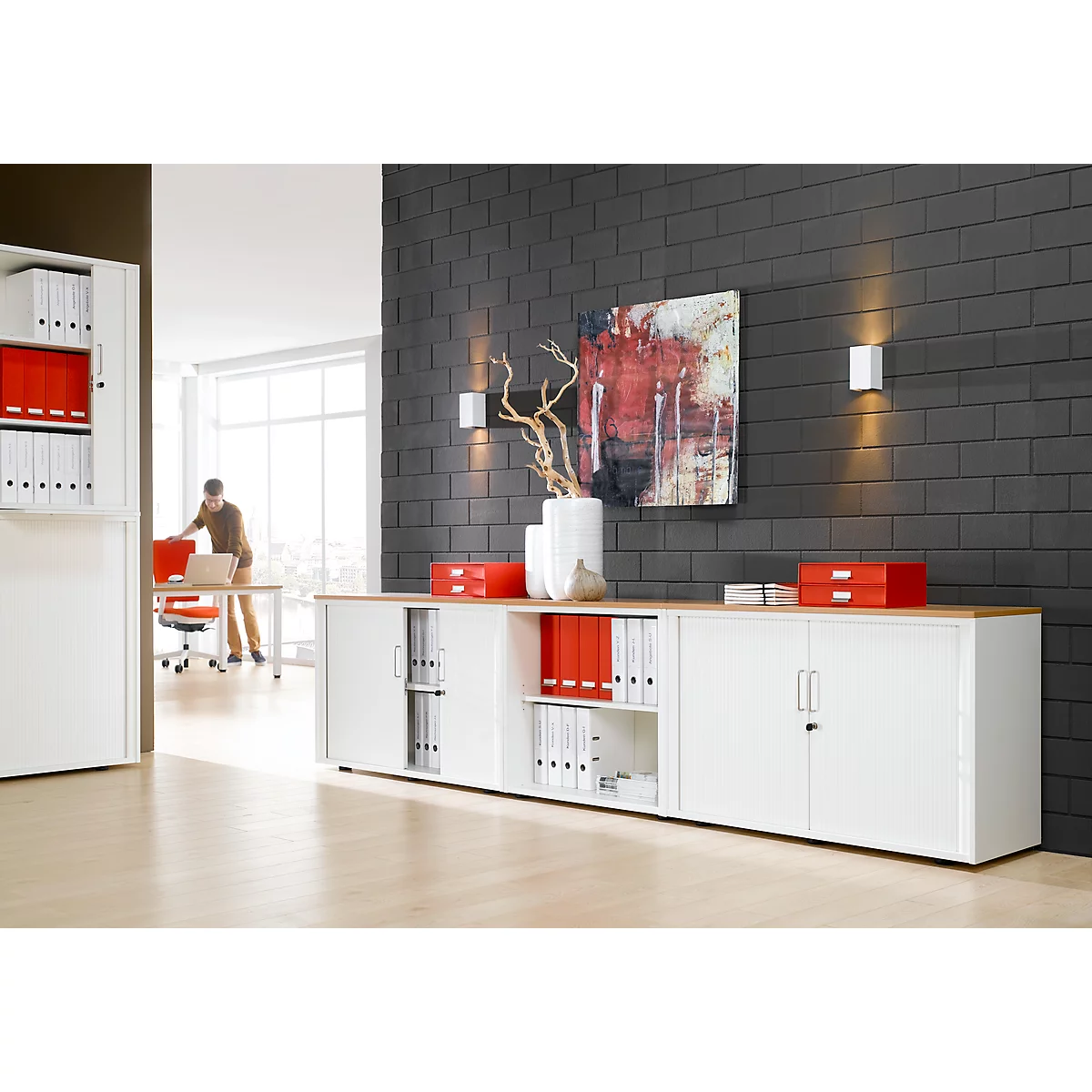 Office with white cabinets, red files, a person, and art on a gray wall. Mood: modern.