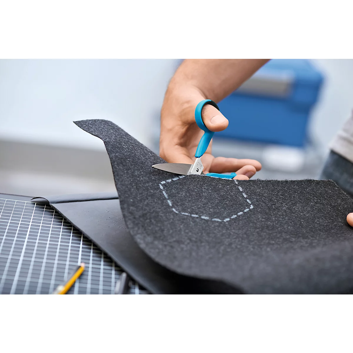 Hände schneiden grauen Filzstoff mit blauer Schere entlang einer gestrichelten Linie zu.