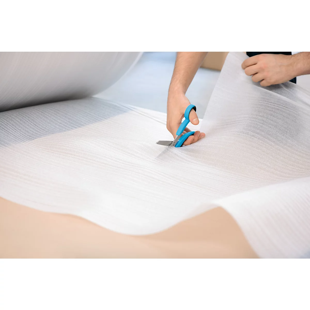 Eine Person schneidet mit einer blauen Schere weißes Verpackungsmaterial zu.