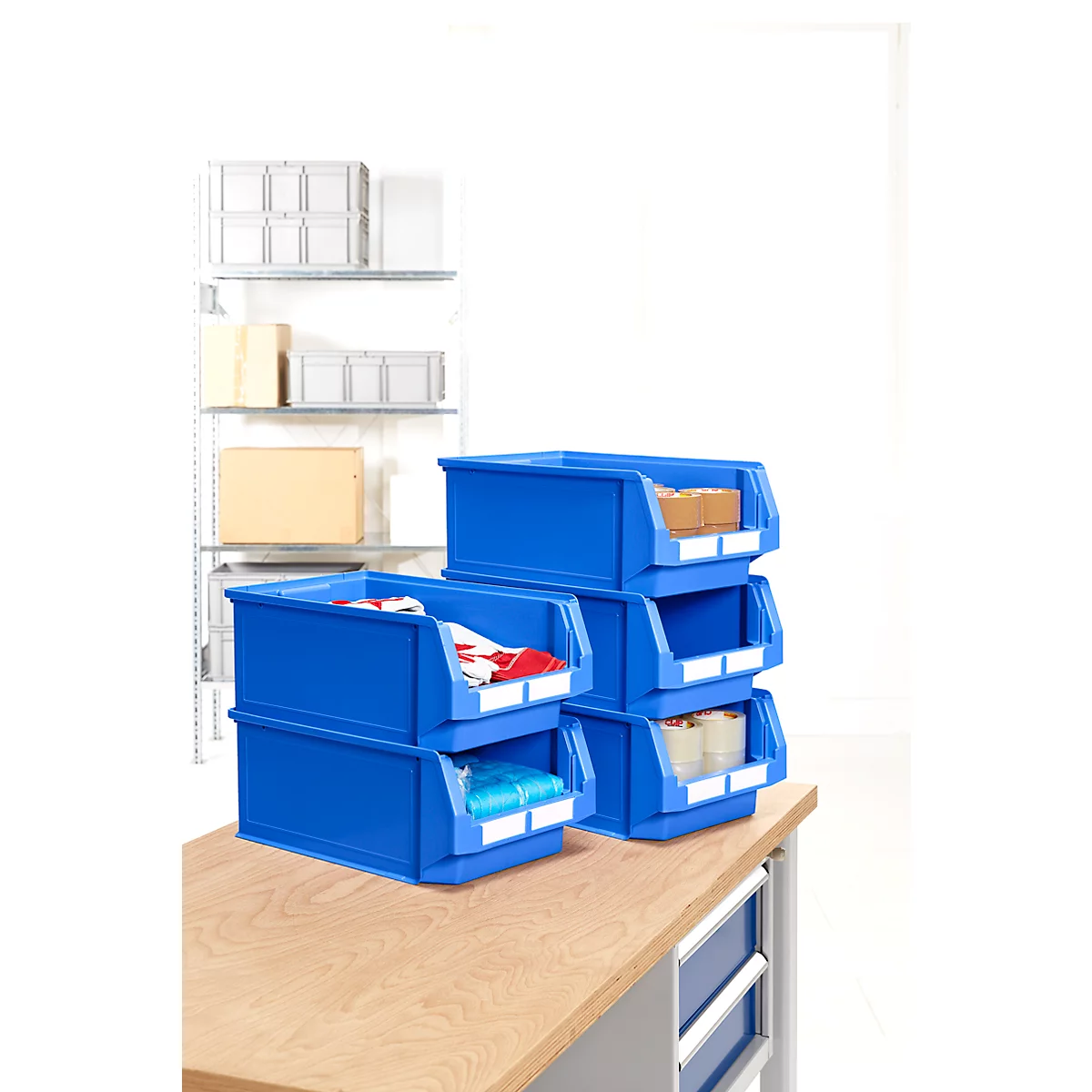 Blaue Kunststoffboxen, gefüllt mit verschiedenen Materialien, auf einem Holztisch. Im Hintergrund Regal mit weiteren Boxen.