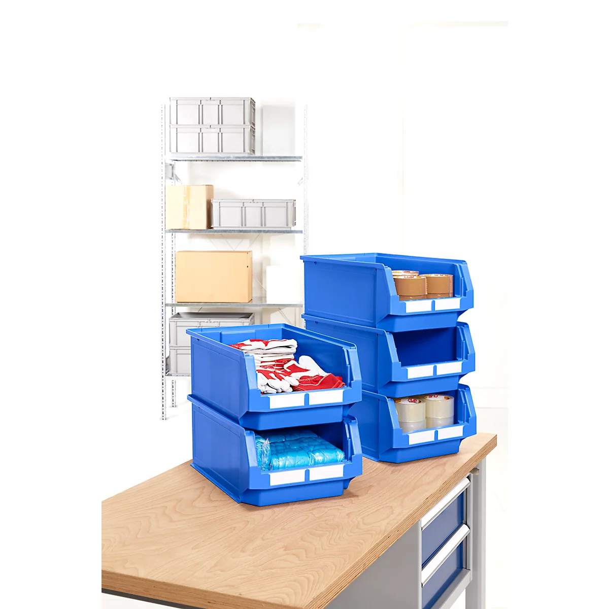 Blaue Lagerboxen mit Inhalten wie Handschuhen und Rollen auf Holztisch. Im Hintergrund Regale mit Kisten.
