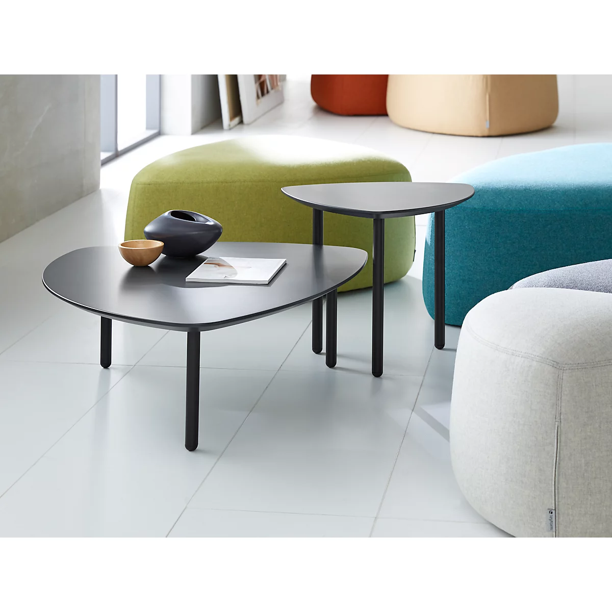 Two black triangular side tables with a book, a bowl, and a vase. Colorful cushions in the background.