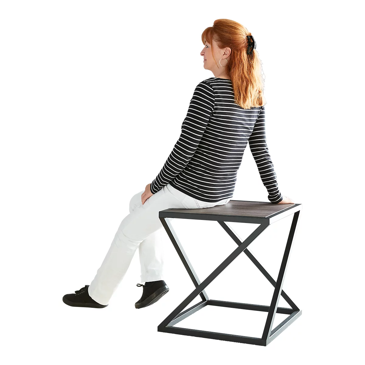 Woman sitting on square side table with black metal frame. She wears striped shirt, white trousers.