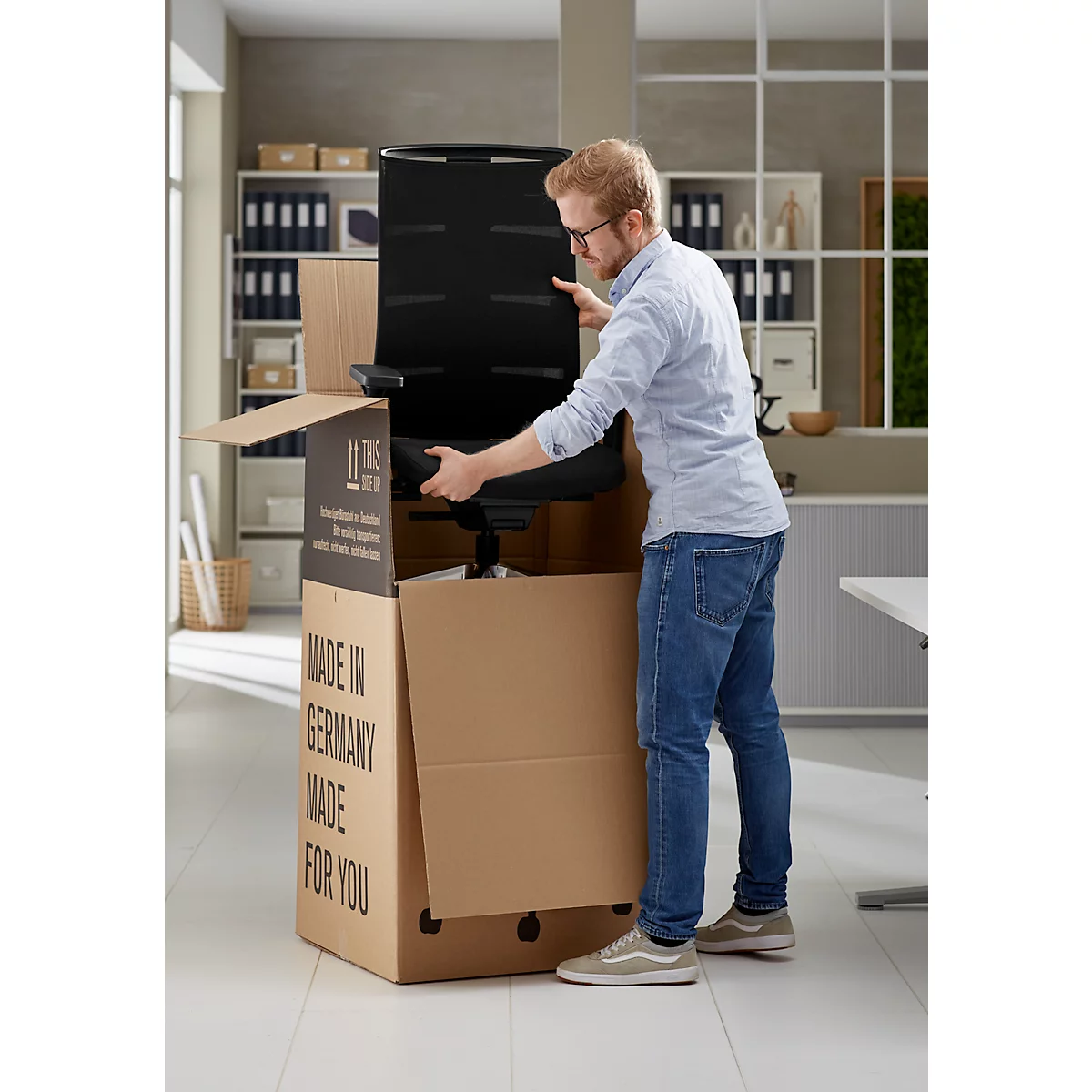 Un homme assemble une chaise de bureau noire à partir d'un carton. Le carton porte l'inscription "Made in Germany".