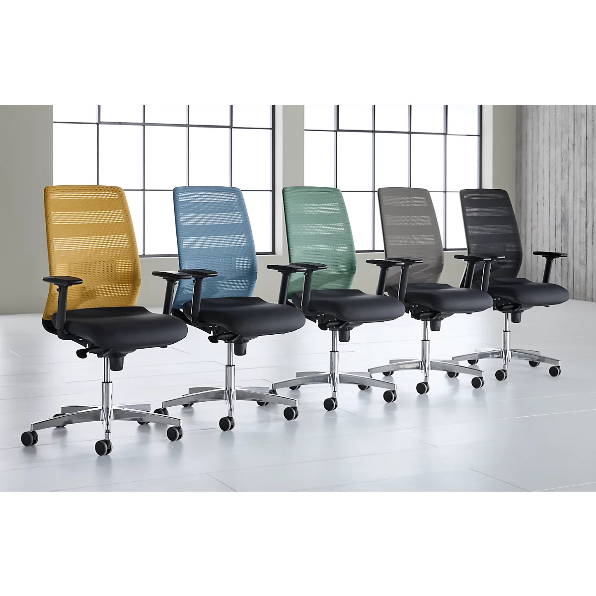 Cinq chaises de bureau avec dossiers en filet colorés devant des fenêtres. Les chaises sont sur roulettes et ont des sièges noirs.