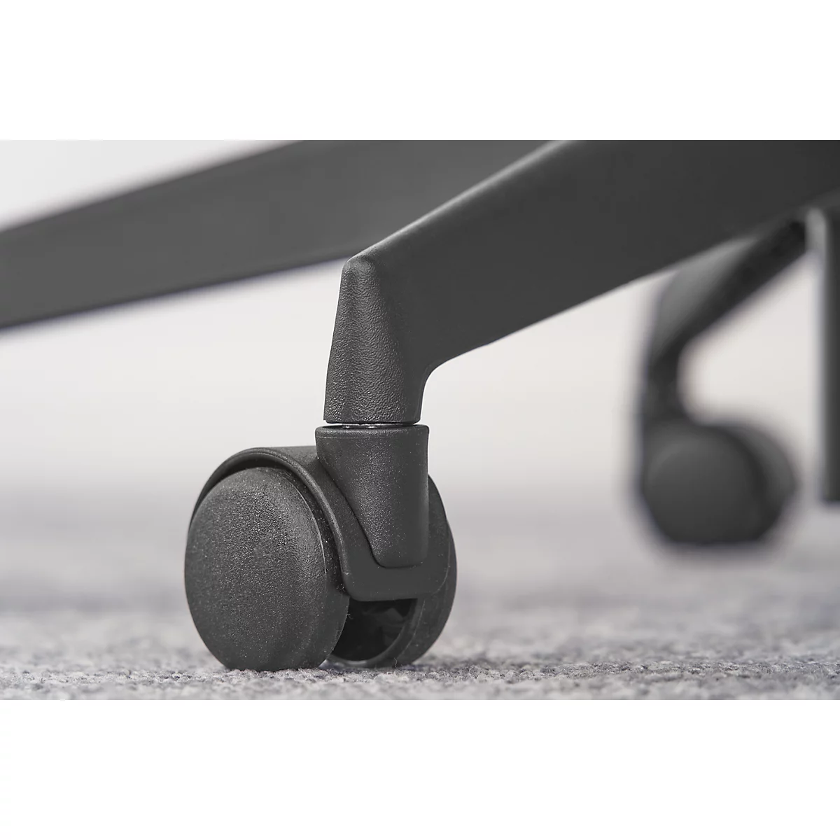 Gros plan sur une roulette noire en plastique d'une chaise de bureau sur une moquette grise.