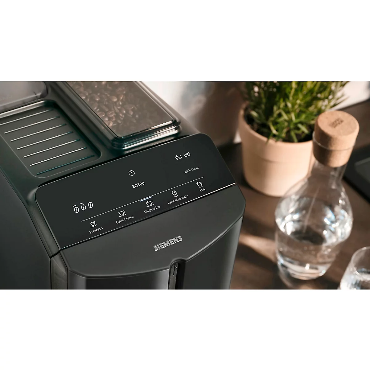 Nahaufnahme eines schwarzen Kaffeevollautomaten. Bedienfeld mit Tasten für Espresso, Cappuccino, Latte Macchiato, etc.. Im Hintergrund: Vase mit Wasser.