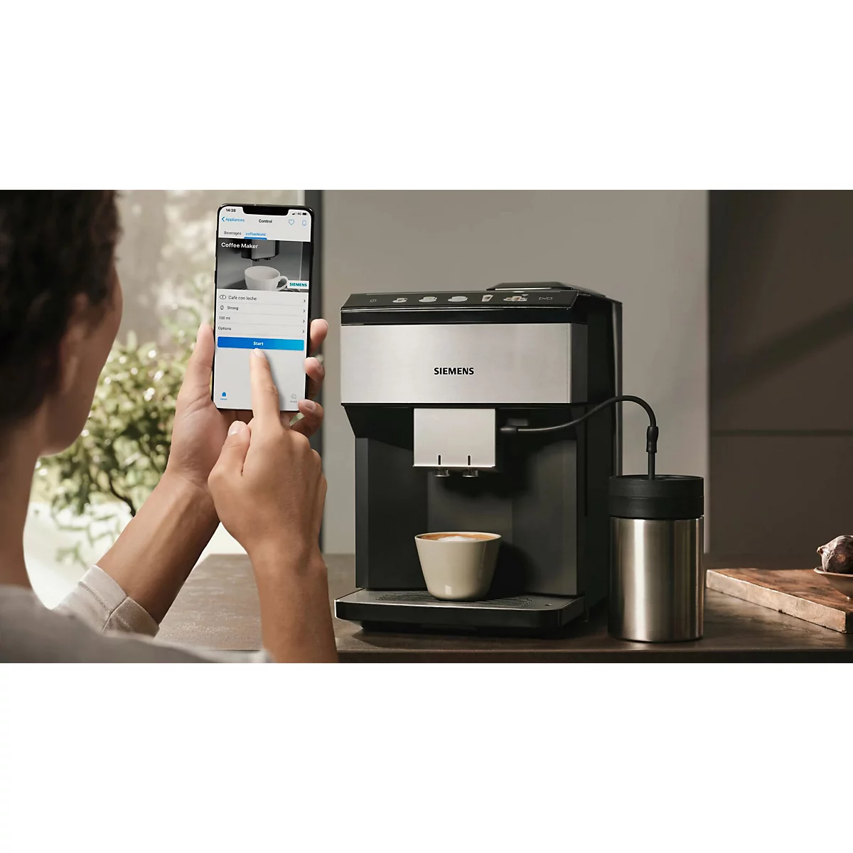 Person bedient Kaffeemaschine via Smartphone. Auf dem Tisch stehen Kaffeemaschine, Tasse, Thermoskanne.