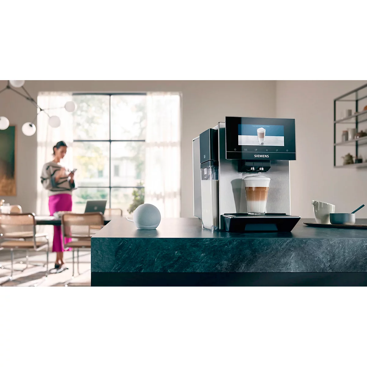 Kaffeemaschine mit Milchkaffee vor einer Frau, die auf ihr Handy schaut.