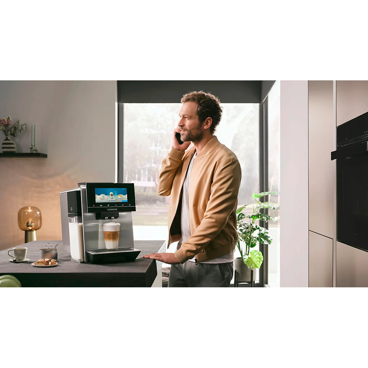 Mann telefoniert neben Kaffeemaschine, Milchkaffee zubereitend.