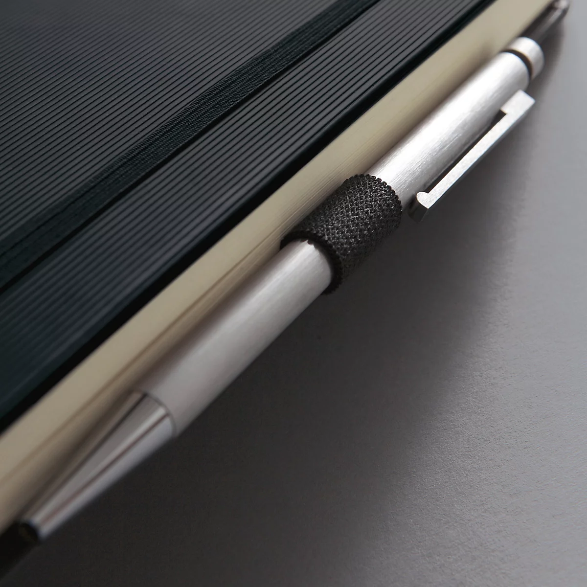 Gros plan : stylo argenté inséré dans un cahier. Des lignes sombres structurent les pages, avec une couverture claire à côté.