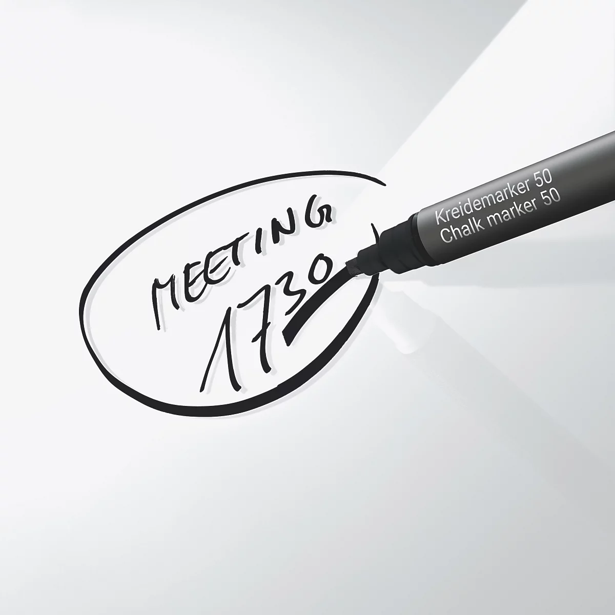 Een zwarte pen schrijft op een wit oppervlak. Het schrijft "Meeting 1730" in een ovale vorm. Op de pen staat "Kreidemarker 50".