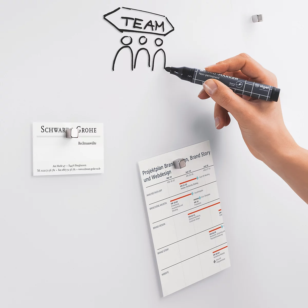 Hand tekent "Team" op whiteboard; visitekaartje en notitievel bevestigd.