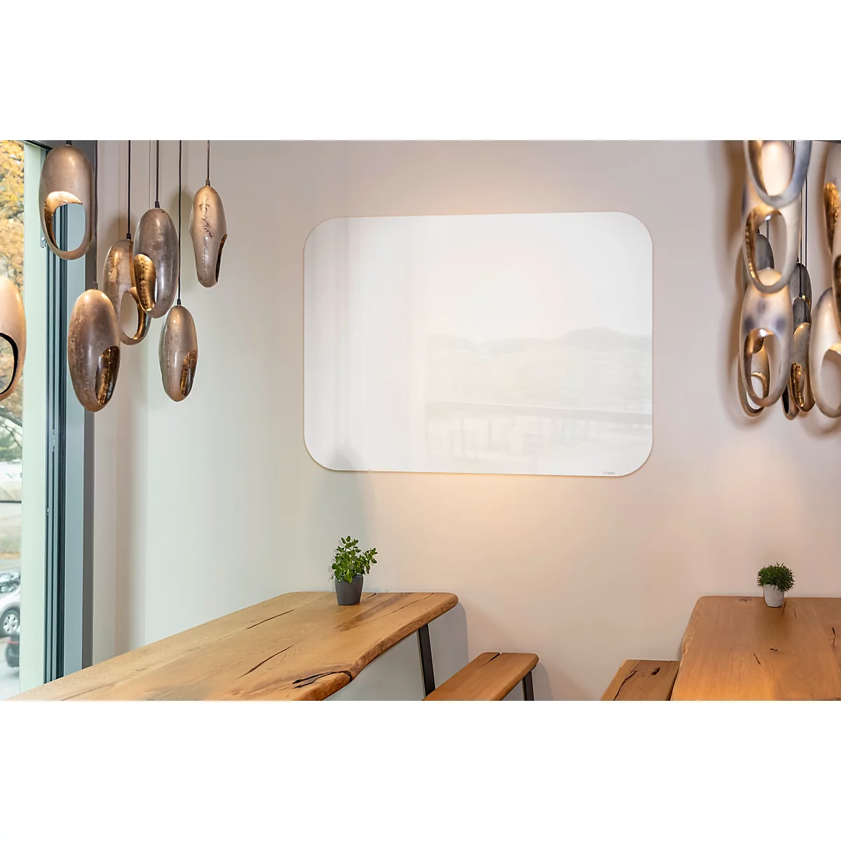 In een café hangt een rechthoekige spiegel aan een crèmekleurige muur. Daaronder staat een tafel met een kleine potplant.