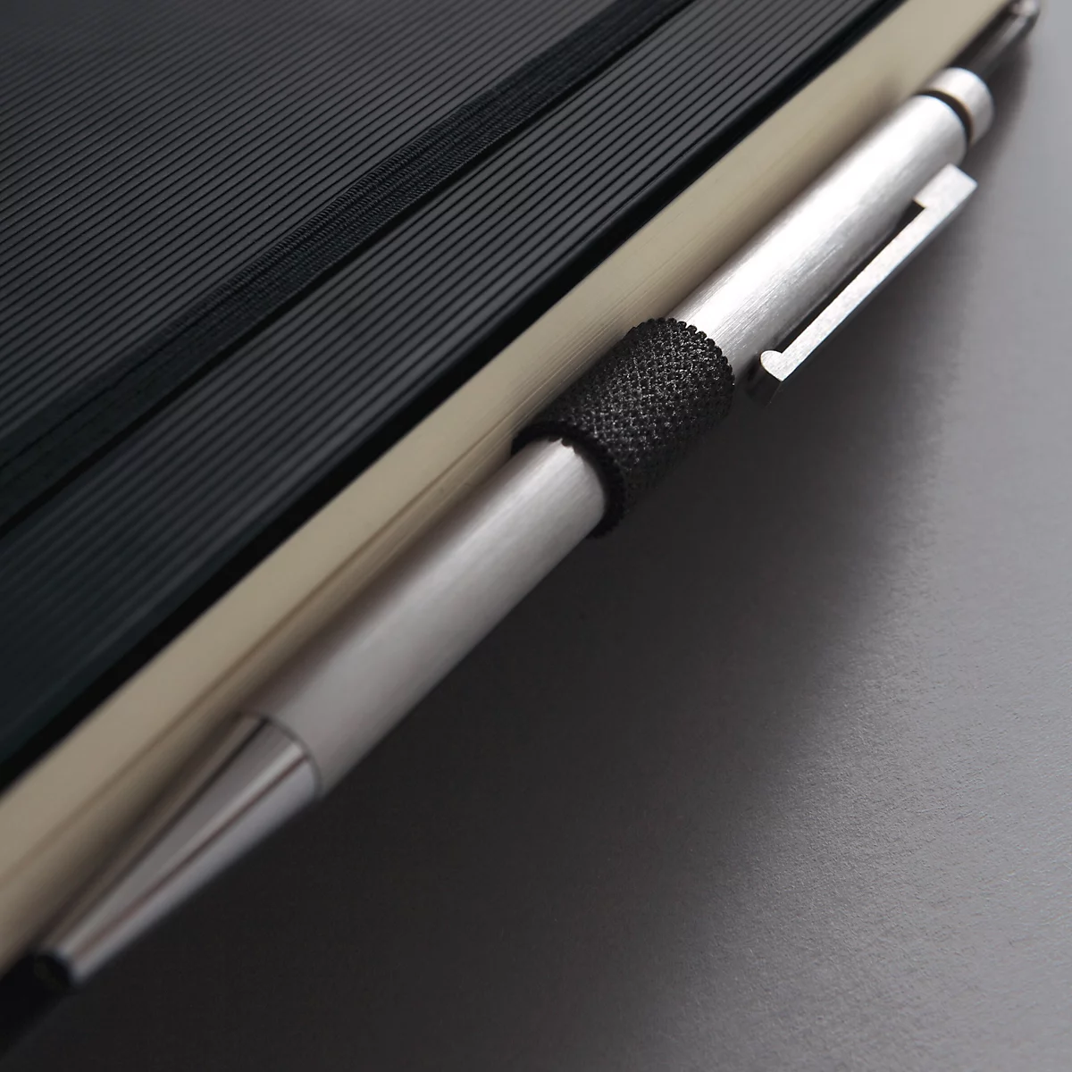 Close-up van een notitieboek met zwarte kaft en zilveren pen. De pen zit in de kaft.