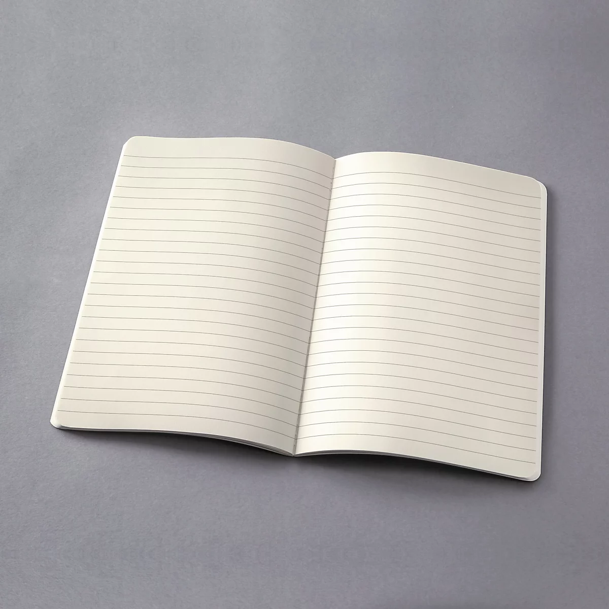 Un carnet ouvert avec des lignes sur une surface grise. Les pages crème sont vierges.