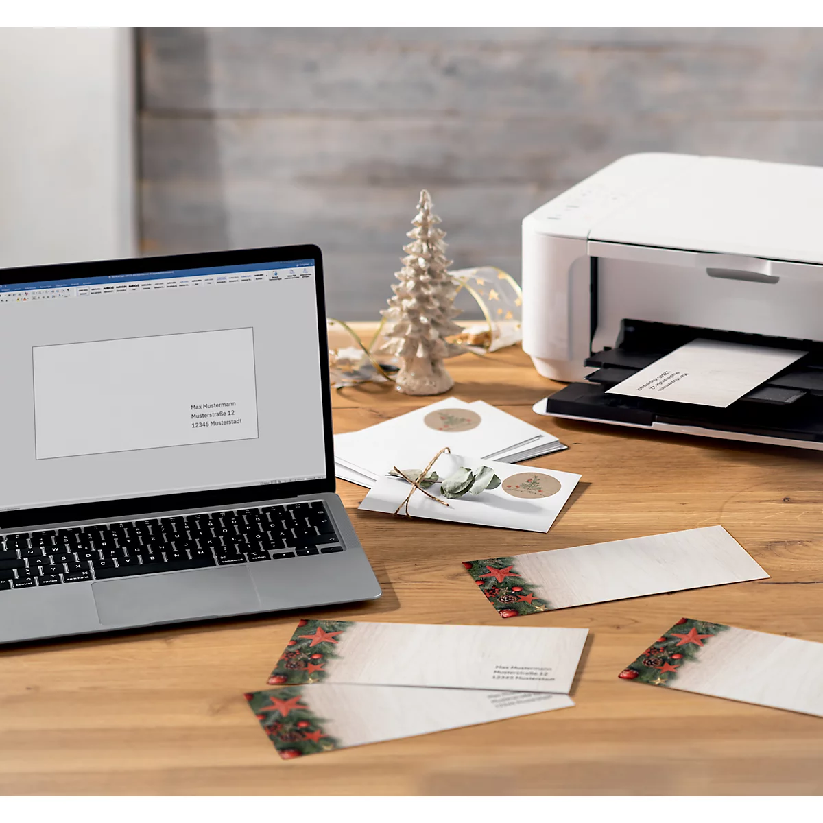 Ordinateur portable et imprimante sur une table en bois. Des cartes de Noël sont imprimées. Sapin de Noël en arrière-plan.