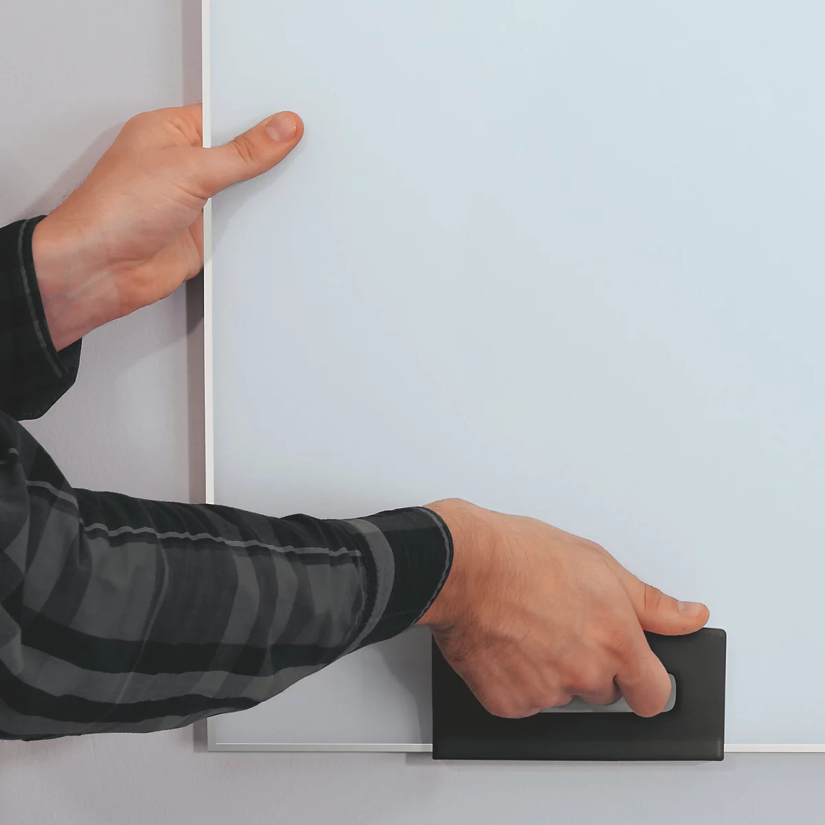 Hände halten eine weisse Tafel. Eine Hand hält die Tafel von oben, die andere greift einen schwarzen Griff.