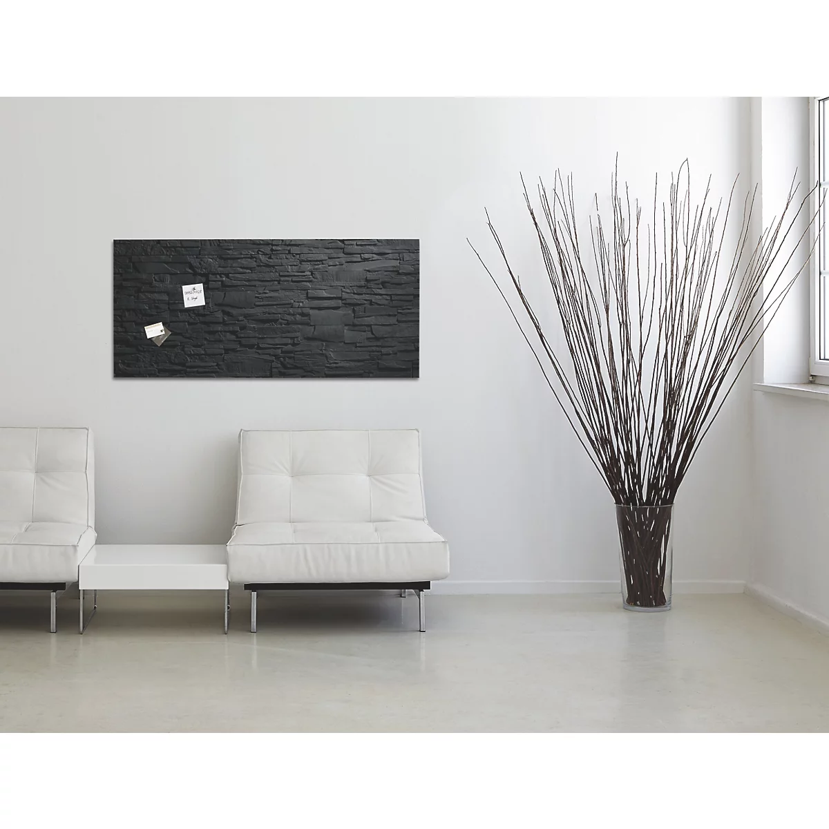 Ein schwarzes Wandboard mit Notizen, zwei weiße Sofas, eine Vase mit Zweigen und ein Fenster.