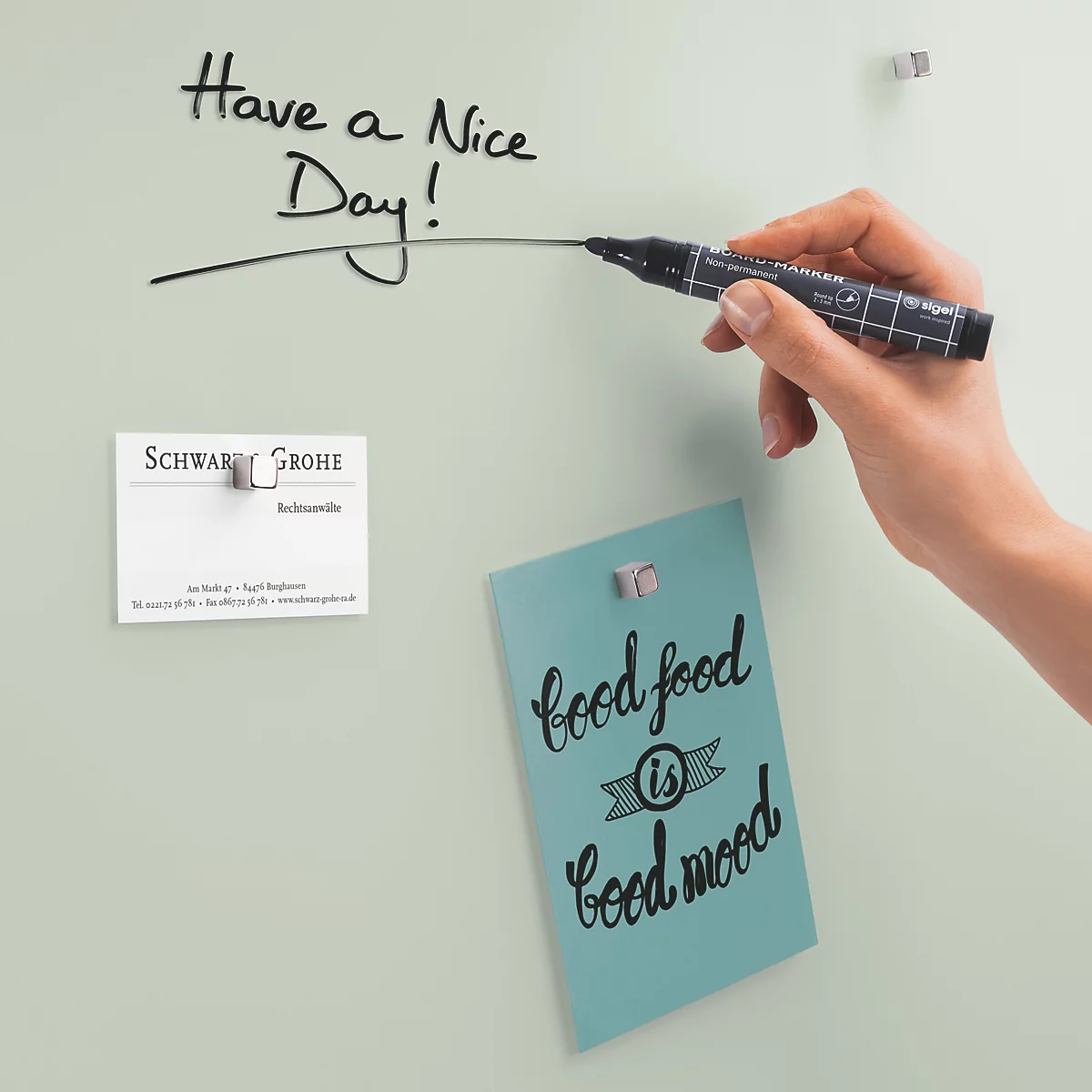 Eine Hand, die mit einem schwarzen Marker "Have a nice day!" auf eine helle Tafel schreibt. Auf der Tafel hängen Notizen.
