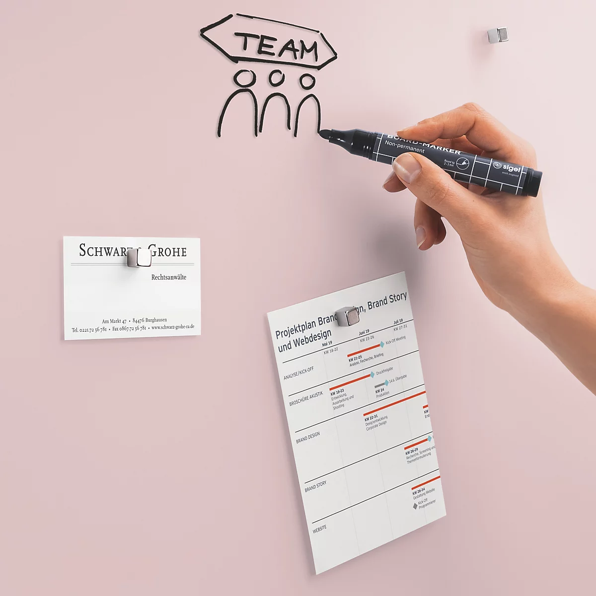 Hand zeichnet "Team" an eine Tafel, Visitenkarte und Notizen sind angeheftet.