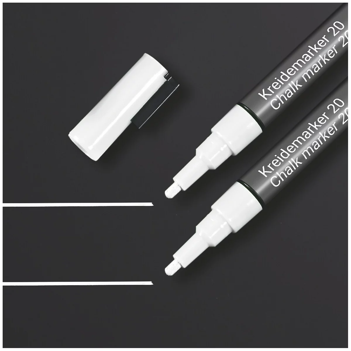 Twee witte krijtstiften liggen op een zwart oppervlak, naast de dop van een stift. Daaronder twee witte lijnen.