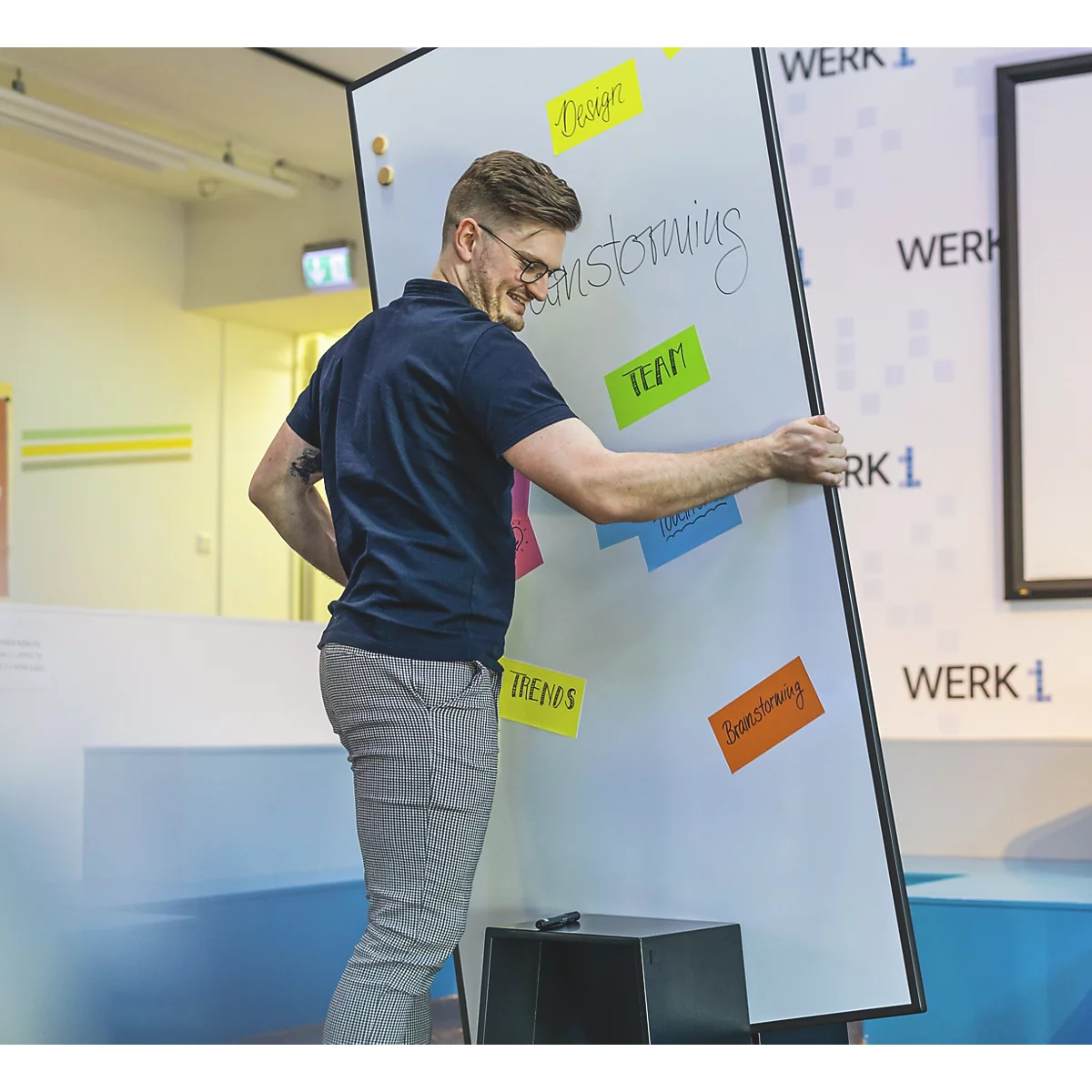 Een man houdt een whiteboard vast met aantekeningen. Op het bord staat "Brainstorming". Stickers met "Design", "Team" en "Thema's" zijn bevestigd.