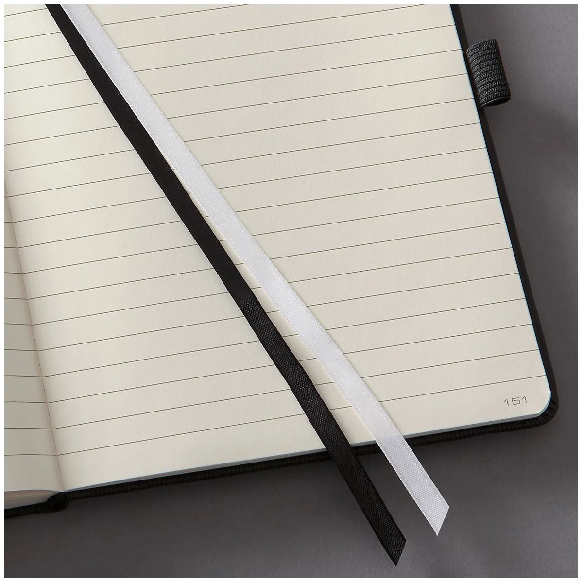Open notebook with lined pages. Black and white ribbons lie on the pages.