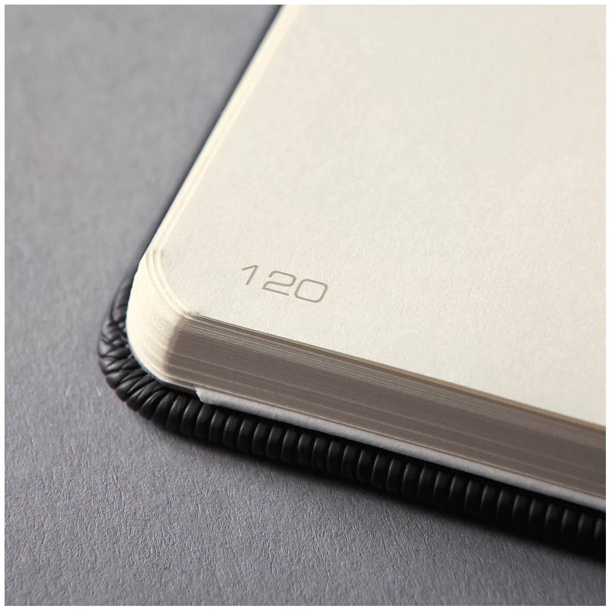Close-up of a notebook with the numbers 120 on an ivory page. The binding is black and wavy.
