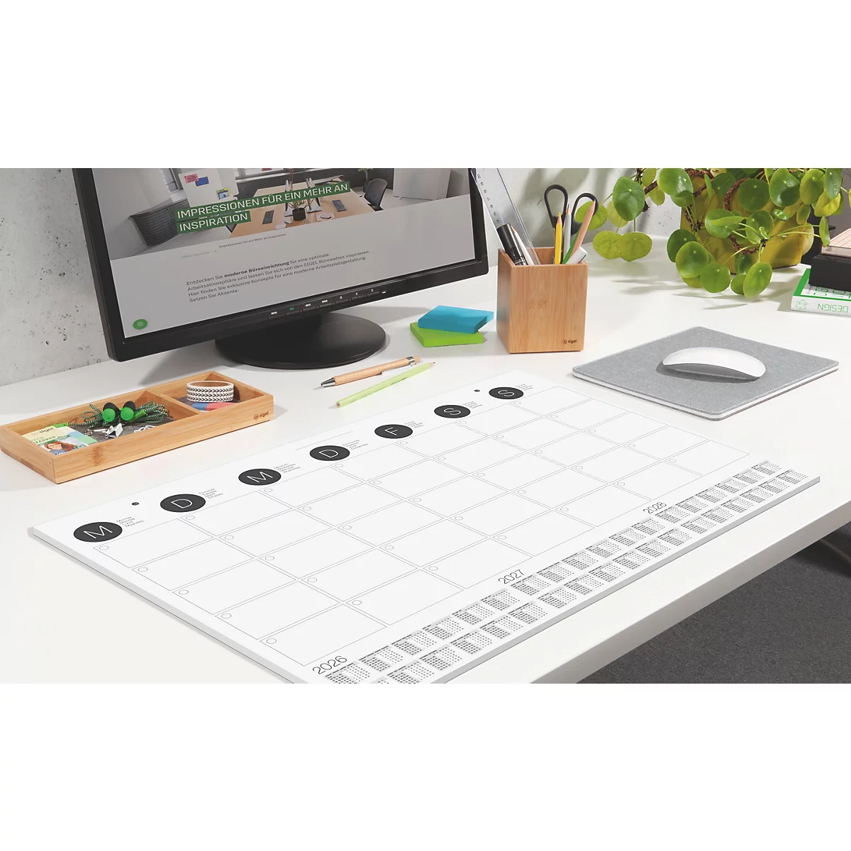 Schreibtisch mit Monitor, Kalender, Mauspad, Stifthalter und Pflanze. Der Kalender hat Monatsnamen und ein Raster.