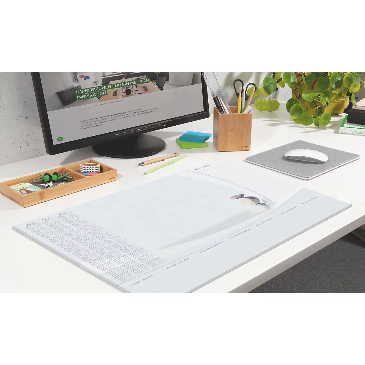 Schreibtisch mit Monitor, Maus, Tastaturabdeckung und Büroutensilien.