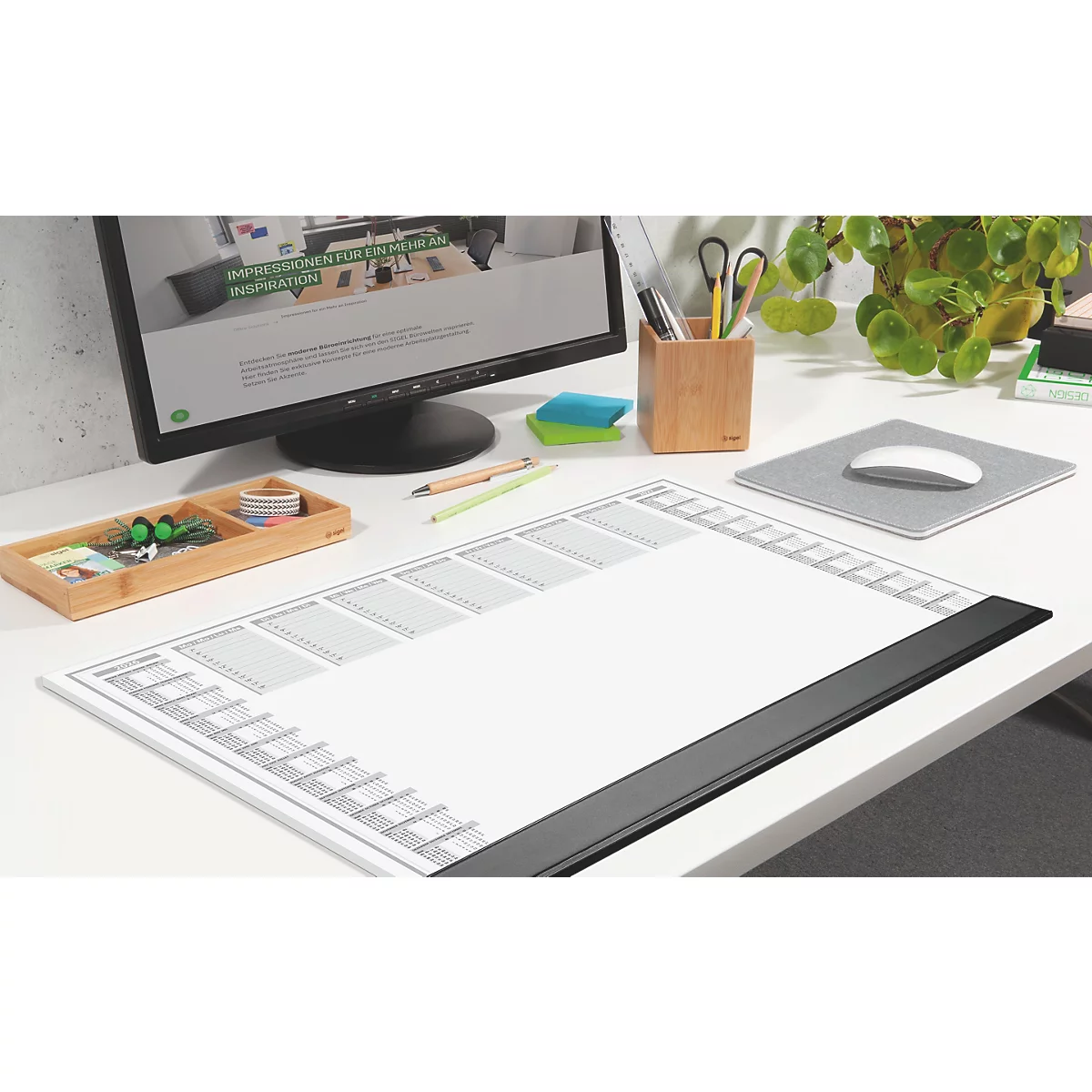 Schreibtisch mit Monitor, einer weißen Zeichenunterlage und Bürozubehör.