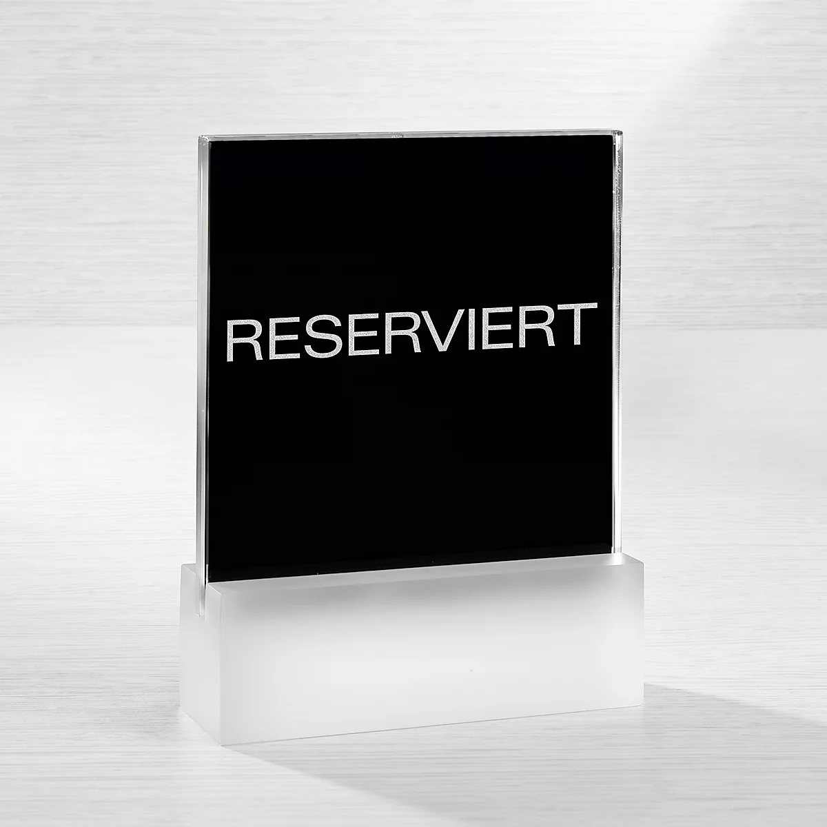 Ein schwarzes Aufstellschild mit der weissen Aufschrift RESERVIERT auf einem milchig-transparenten Sockel.