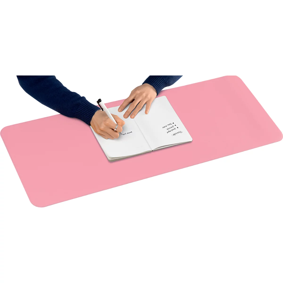 Person schreibt in Notizbuch auf rosa Schreibtischunterlage. Im Notizbuch sind Notizen zu sehen.