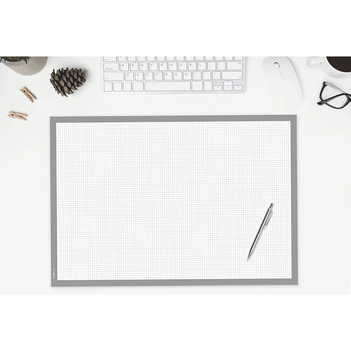 Draufsicht auf einen Schreibtisch mit karierter Schreibunterlage, Tastatur, Maus, Brille, Stift und Deko-Elementen.