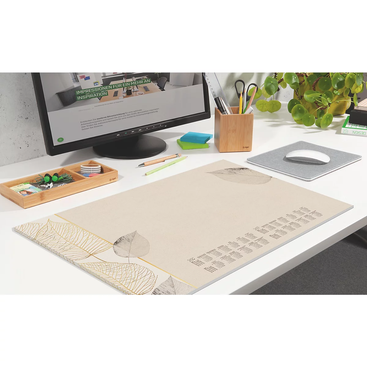 Beige bureau-onderlegger met bladerenpatroon en tekst, omringd door bureau-artikelen.