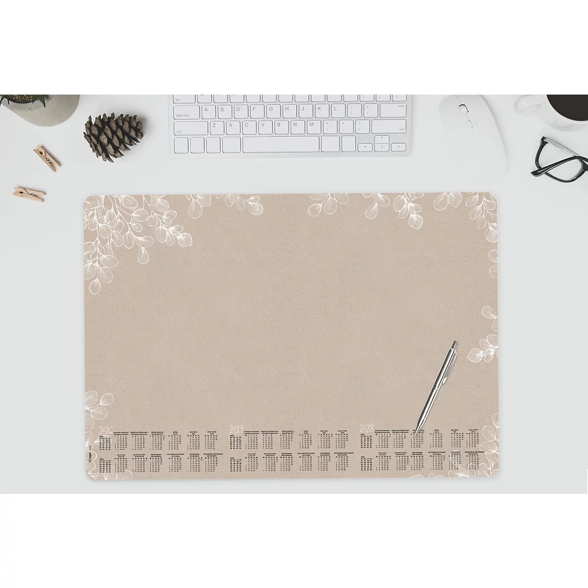 Beige bureau-onderlegger met wit bladerpatroon en kalender. Pen ligt ernaast.
