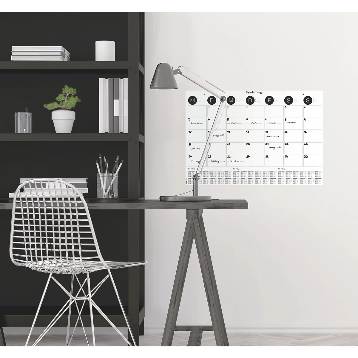 Bureau met lamp en kalender aan de muur, naast een plank en stoel.