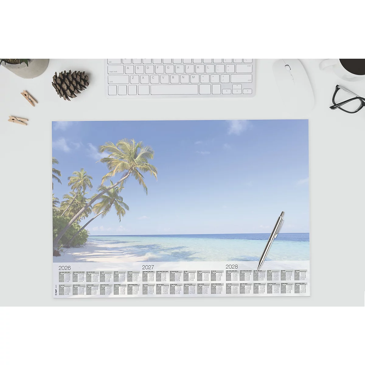 Calendrier avec une scène de plage sur un bureau blanc. Stylo et accessoires informatiques éparpillés.