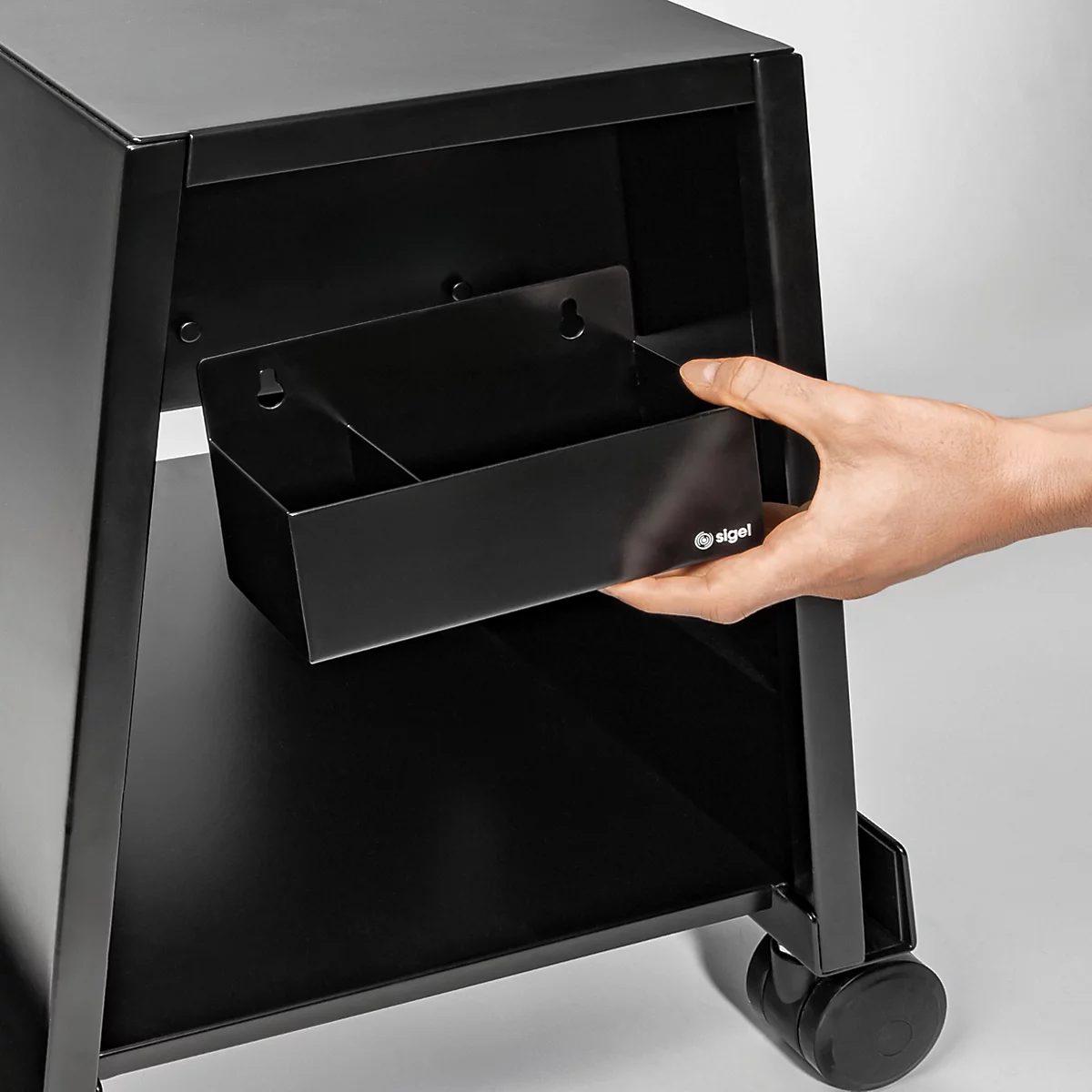 Une personne tenant un tiroir noir sur un chariot noir.