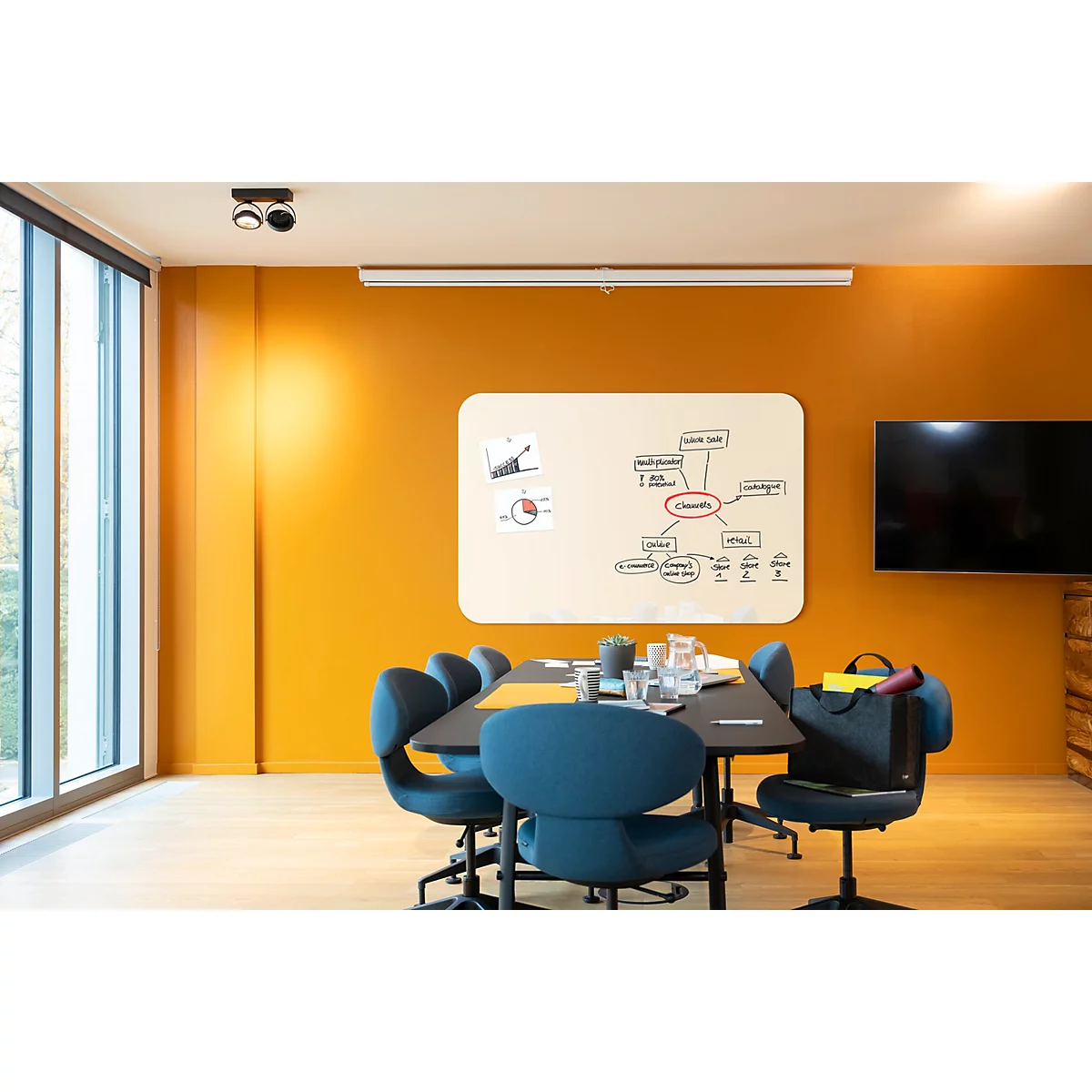 Une salle de conférence avec des murs orange avec une table avec des chaises, un tableau blanc et une télévision.