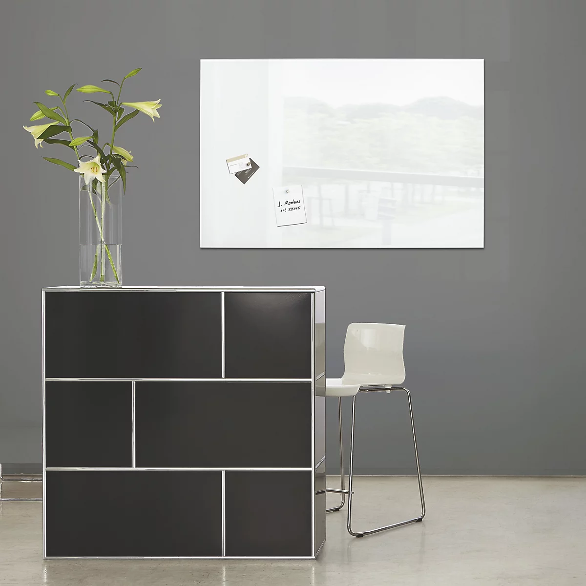 Armoire noire avec cadre blanc, chaise et tableau avec notes. Dans un vase: fleurs blanches.