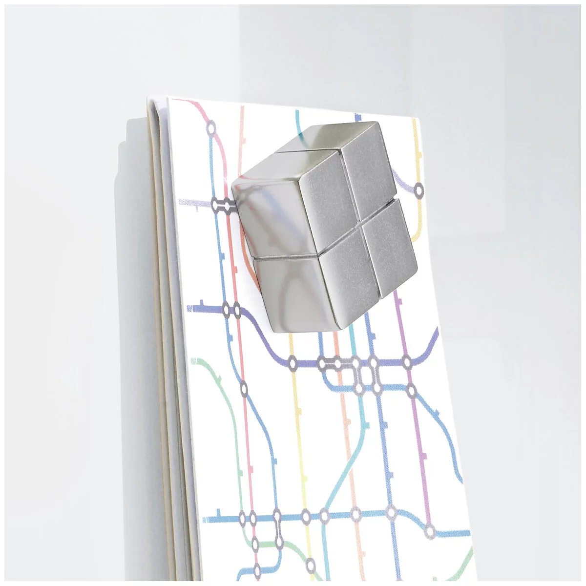 Un cube argenté repose sur un carnet avec des lignes de métro. Le carnet est devant un mur blanc.