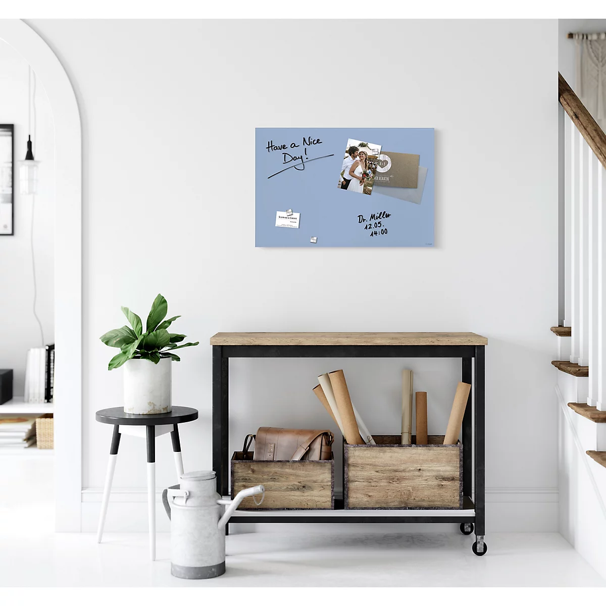 Tableau mémo bleu clair avec notes et photos sur le mur. En dessous, une table avec décoration et une plante.