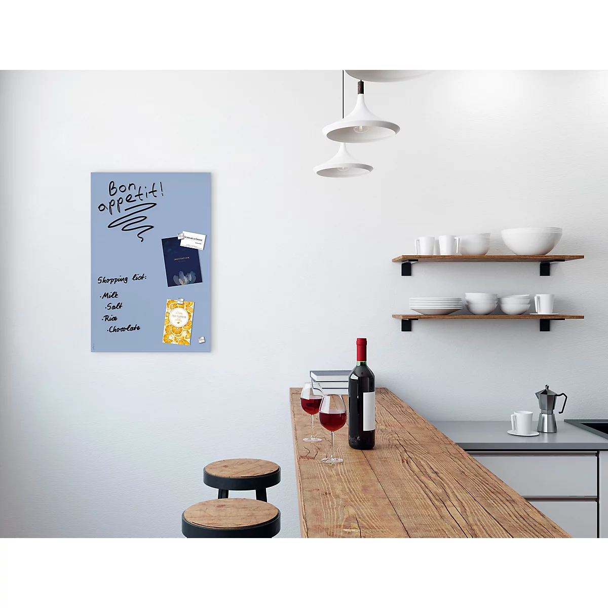 Tableau blanc bleu clair avec l'inscription "Bon appétit!". En dessous, une liste de courses avec lait, sel, beurre, chocolat. Dans la cuisine devant le bar en bois.