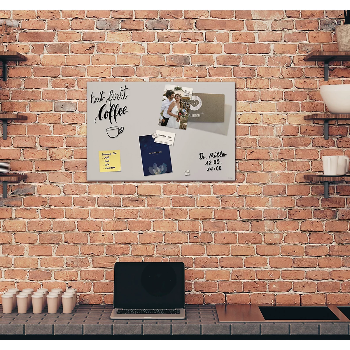 Vue d'un mur de briques avec un tableau d'affichage gris attaché. Le tableau d'affichage contient des notes, des photos et un ordinateur portable.