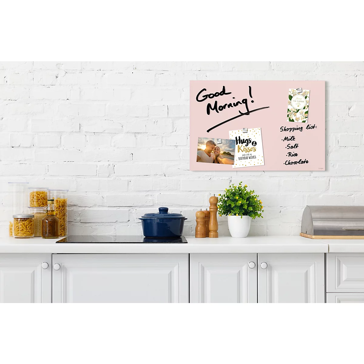Tableau magnétique rose avec des notes et 'Good Morning'. Dans une cuisine, sur une surface blanche, avec des accessoires.
