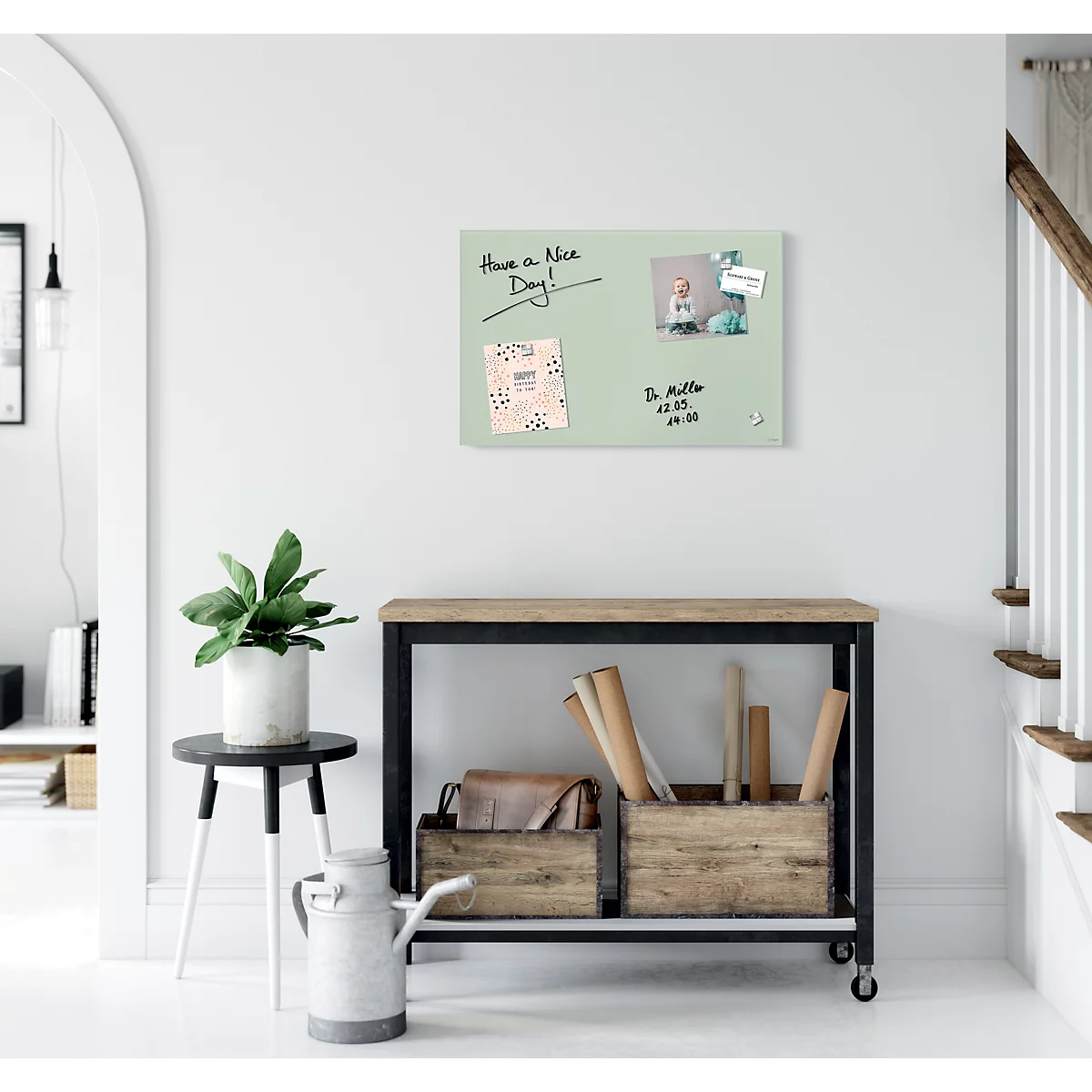 Tableau magnétique vert clair avec des notes et une photo, sur un mur blanc. En dessous, une table avec décor.