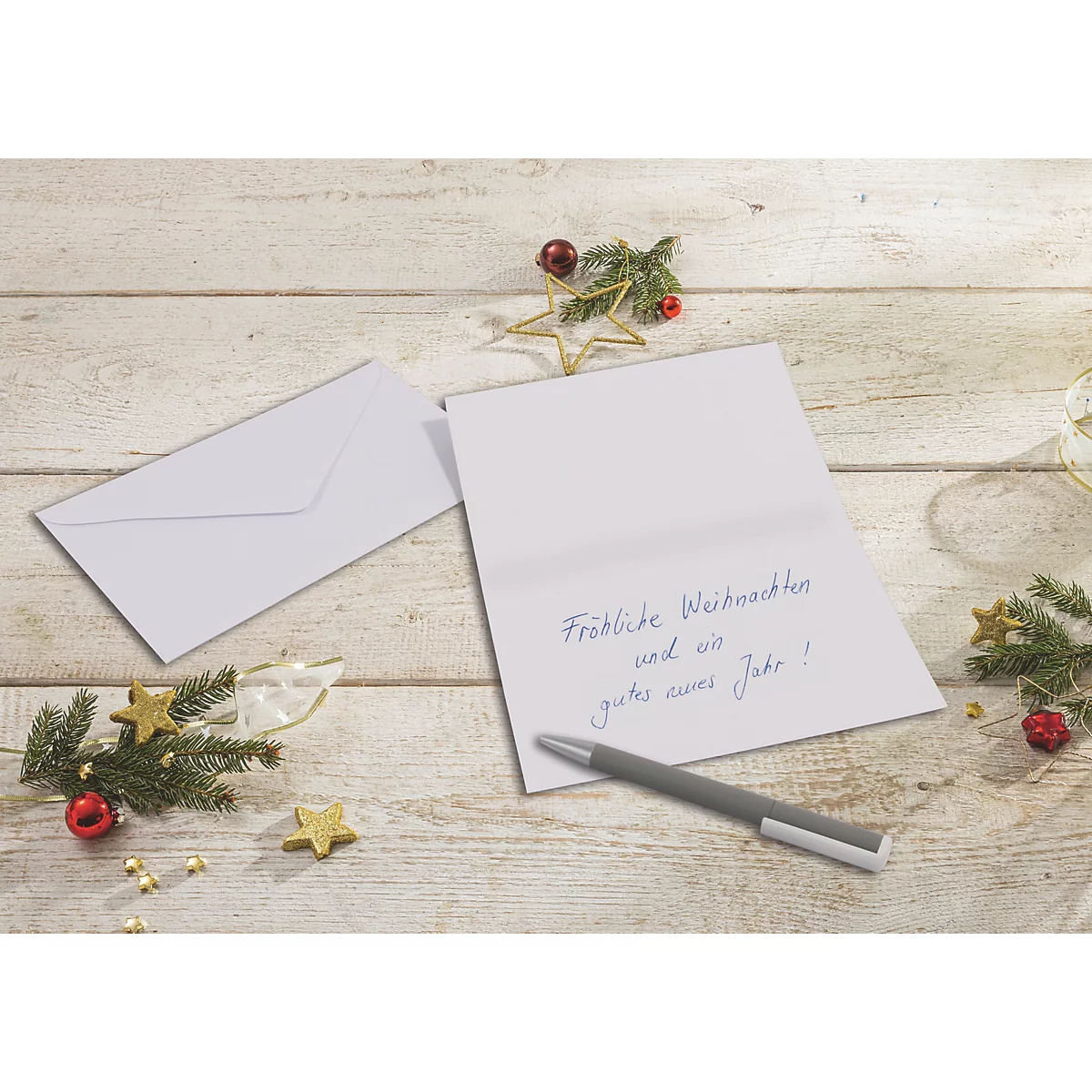 Eine geöffnete Weihnachtskarte mit handgeschriebenem Text liegt neben einem Umschlag und einem Kugelschreiber auf einem Holztisch.