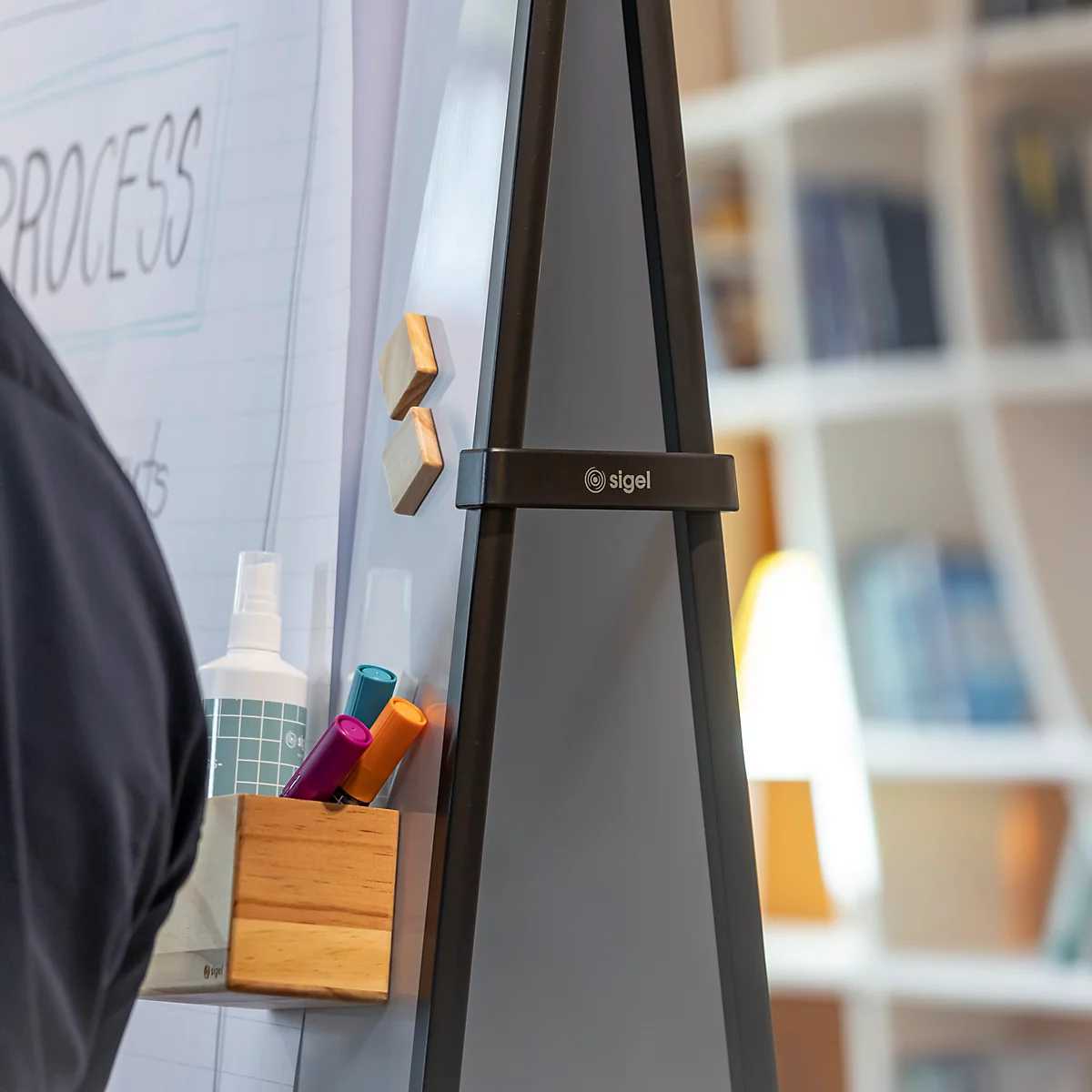 Nahaufnahme eines Sigel Flipcharts mit Holz-Zubehörhalter und Markern vor einem unscharfen Regal.